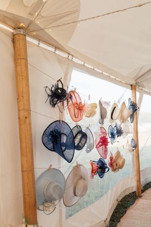 Decorative fascinators and hats hanging on display at a wedding venue under a white tent canopy.