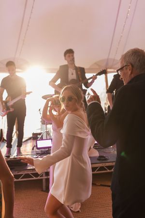 Wedding reception dance party with people dancing under a white tent with stage lighting creating a festive atmosphere.