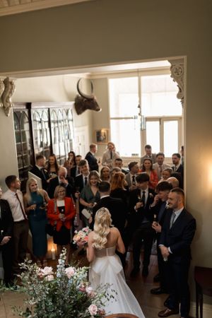 A crowd of wedding guests gather in an elegant indoor venue with mounted animal head decor and floral arrangements.