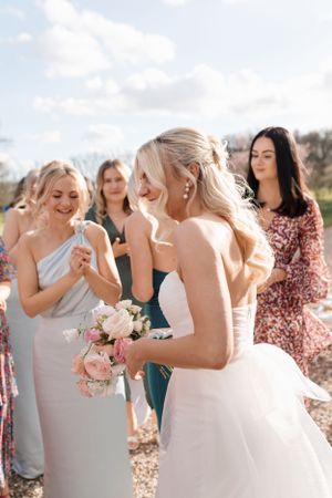 Wedding party with bridesmaids in soft pastel dresses gather outdoors sharing joyful moment during celebration.