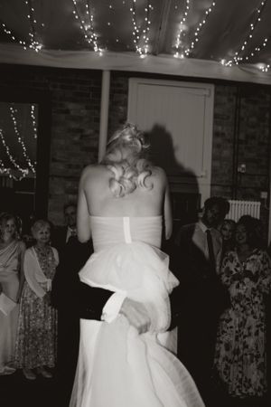 A black and white photo shows the back of a bride in a strapless white dress with decorative twinkle lights above.