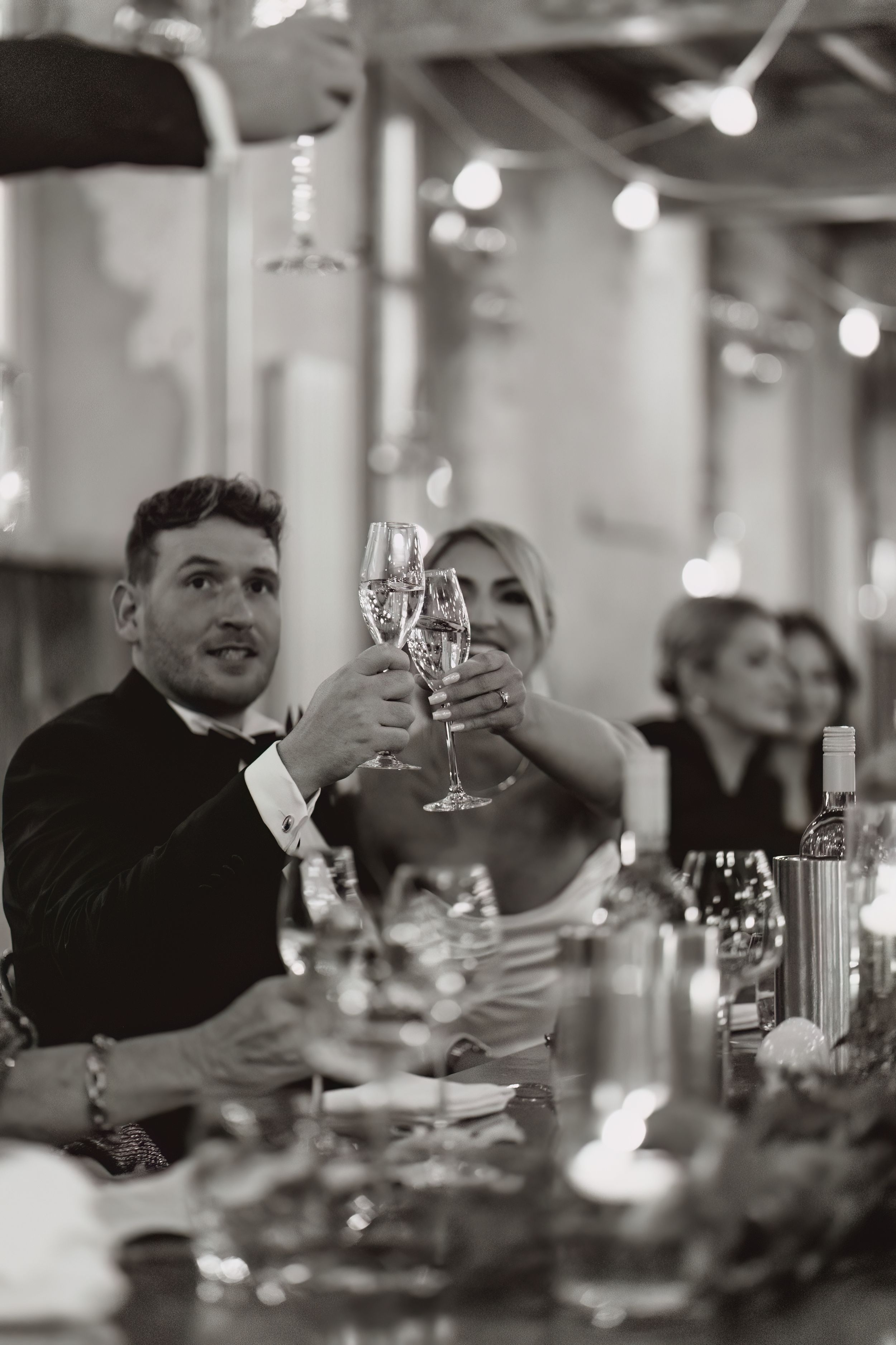 Black and white photo of a wedding toast with champagne glasses at an elegant reception.