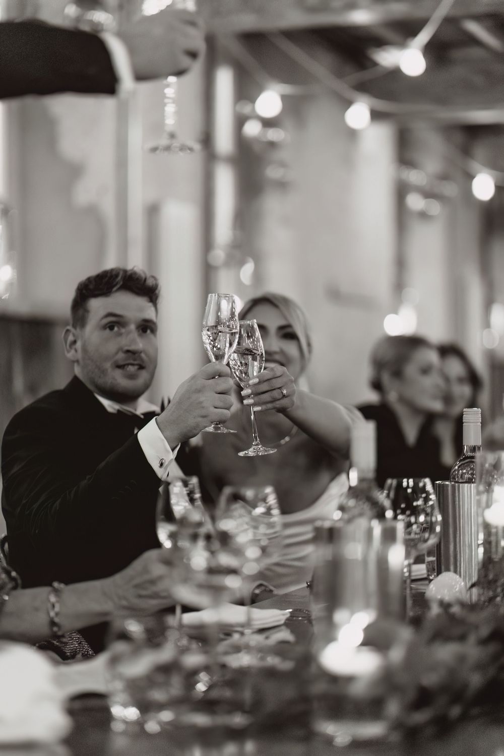 Black and white photo of a wedding toast with champagne glasses at an elegant reception.