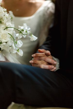 An intimate wedding detail shot of clasped hands next to delicate white flowers.