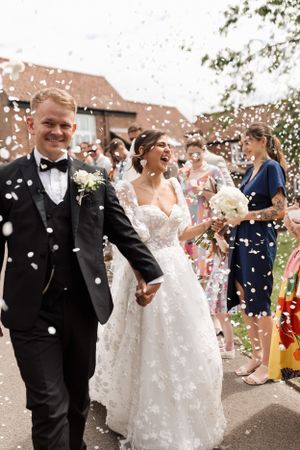 Wedding guests shower confetti on a happy couple outside a rustic brick building.