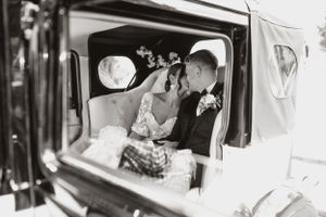A vintage black and white photo of newlyweds sitting in a classic car.
