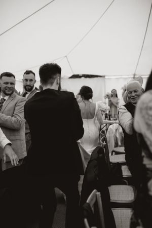 A candid black and white shot of wedding guests enjoying the reception under a tent.