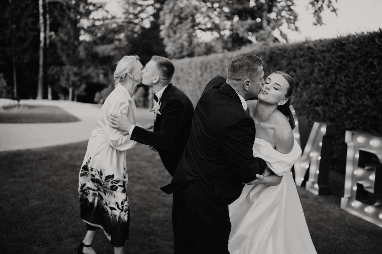 Wedding celebration captured in black and white as guests share drinks outdoors.