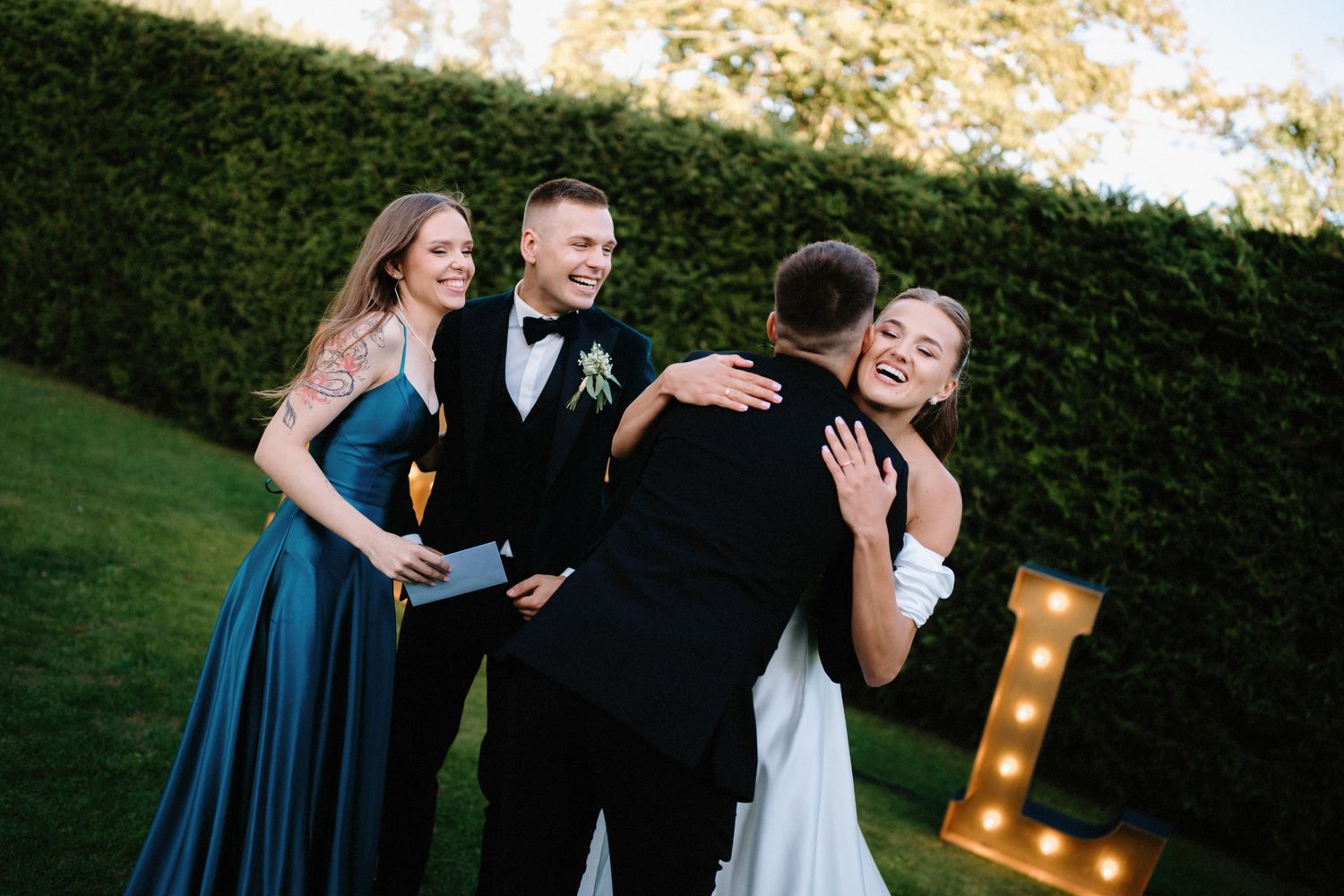 Wedding celebration with guests in navy dresses dancing near illuminated marquee letters.