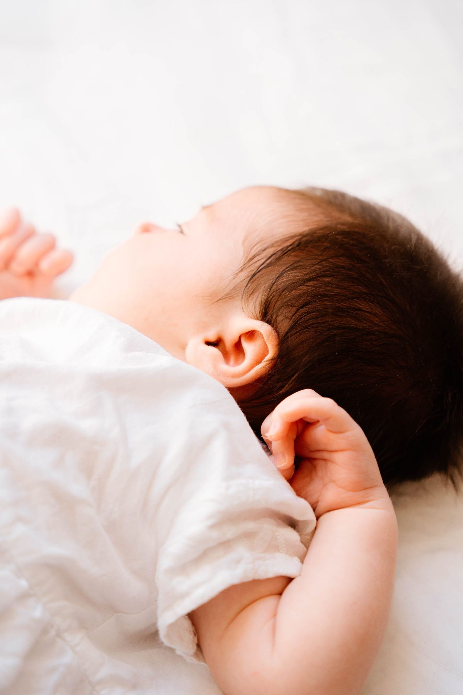 Sleeping baby in white clothing rests peacefully against soft bedding.