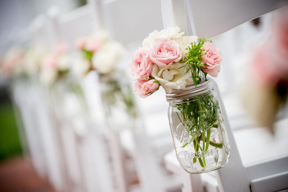 Pink roses and delicate floral arrangements in glass mason jars create an elegant wedding centerpiece display.