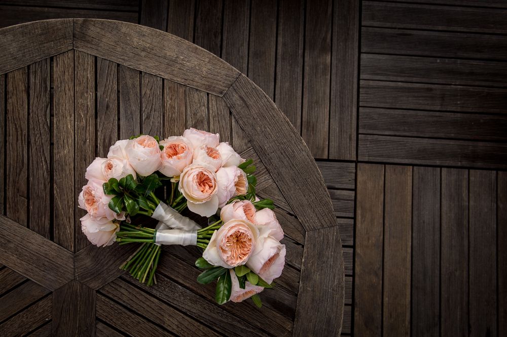A bouquet of pink garden roses rests on a dark wooden bench with slat pattern detail.
