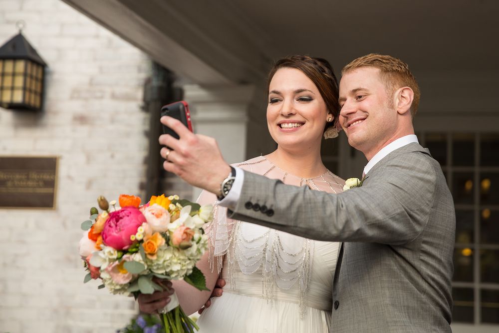 A couple takes a selfie during their wedding celebration while holding a vibrant bouquet.