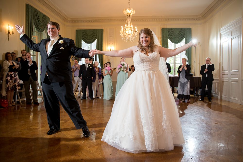 Wedding guests dancing and celebrating in elegant ballroom with hardwood floors and chandeliers.