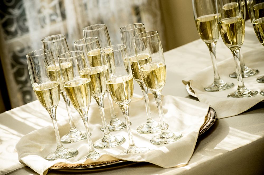 Champagne flutes lined up on white tablecloth at formal wedding reception.