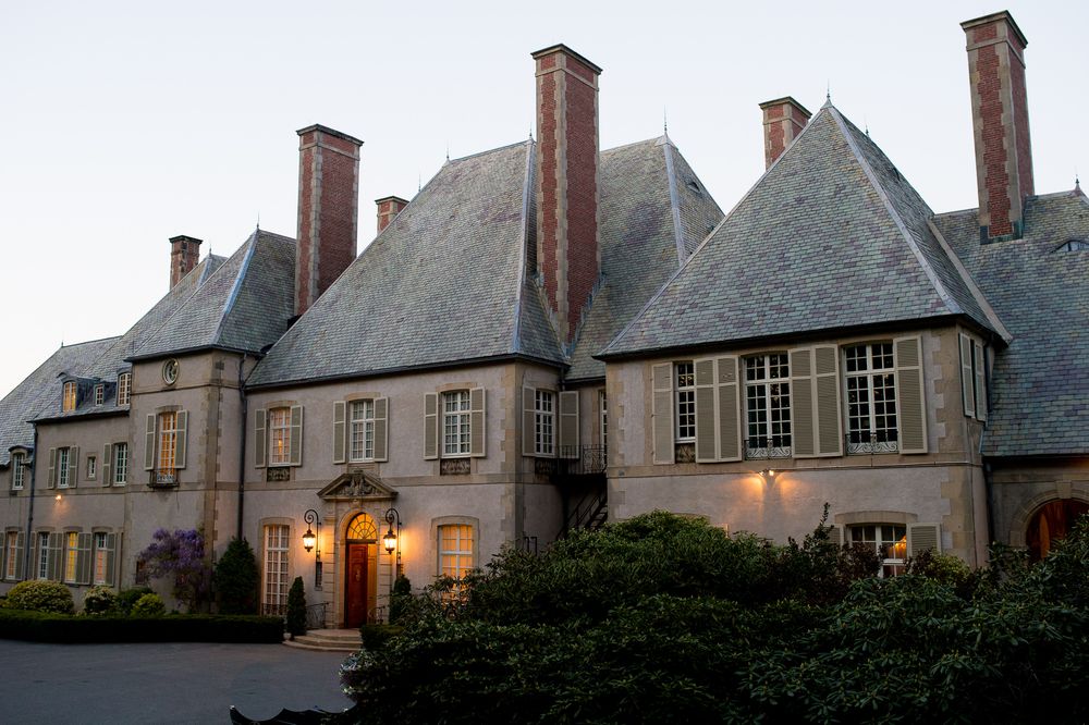 Historic stone manor house with multiple chimneys photographed at dusk.
