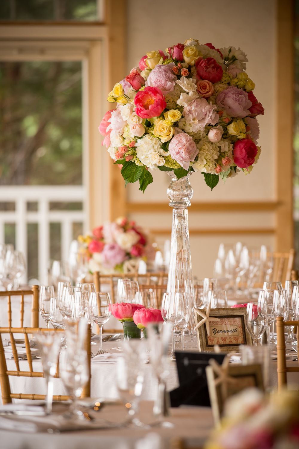 Elegant wedding reception table settings with tall floral centerpieces in crystal vases and gold chiavari chairs.