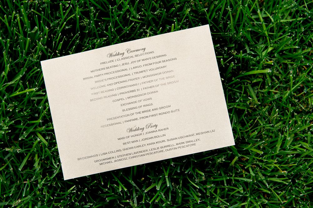 Wedding invitation card with elegant typography laid on green grass.