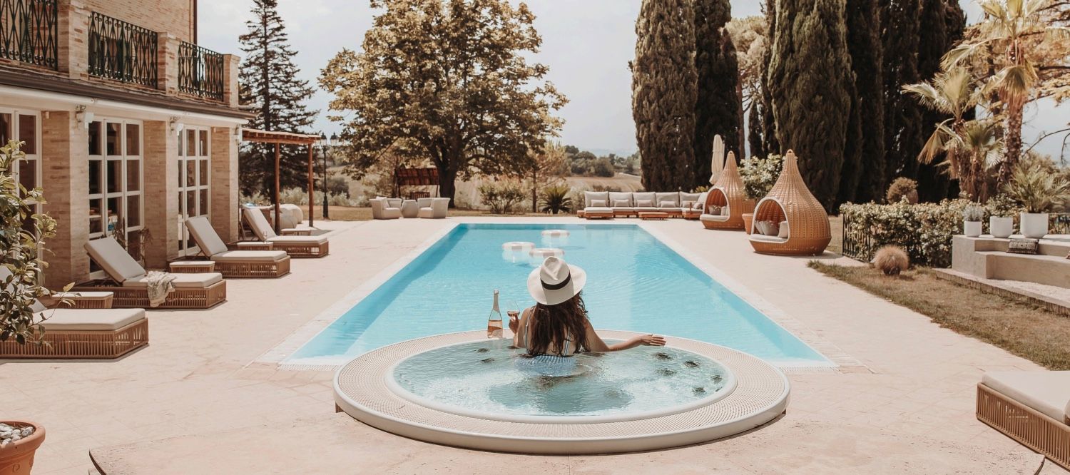 Person relaxing in luxury pool area with lounge chairs and Mediterranean architecture.