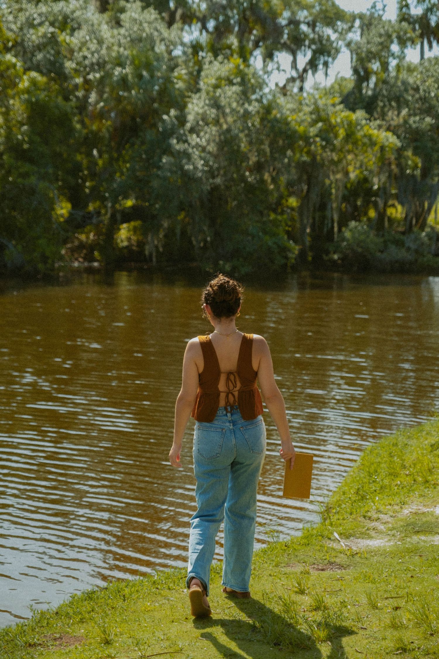 Figure in denim walking along grassy lakeside on a sunny day.