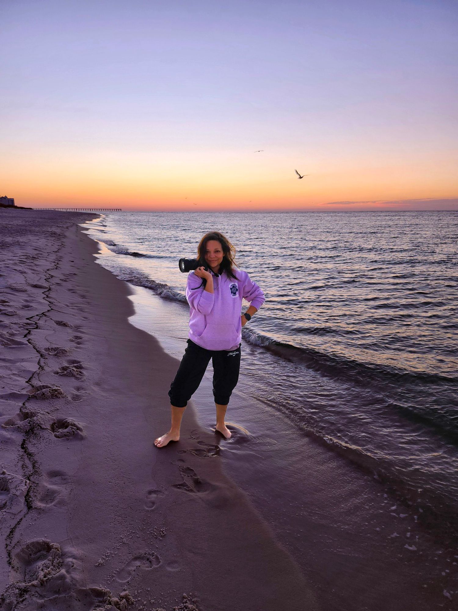 Someone in casual clothes poses playfully on beach at sunset.