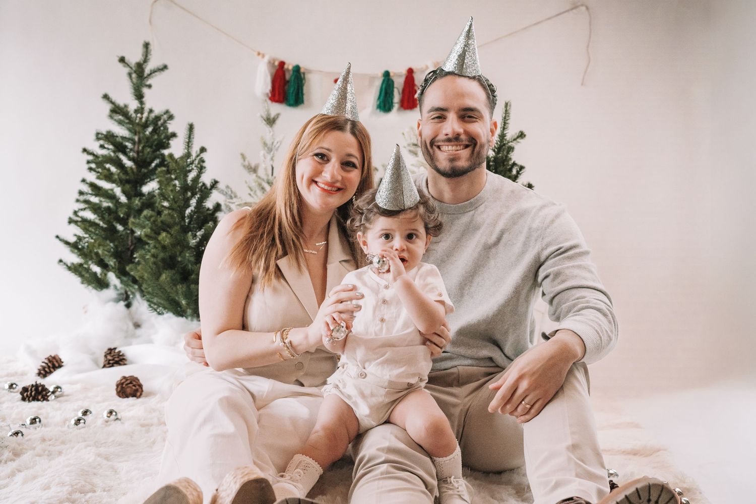A family sits together on the floor in front of a Christmas tree in a bright white room with festive holiday decor.