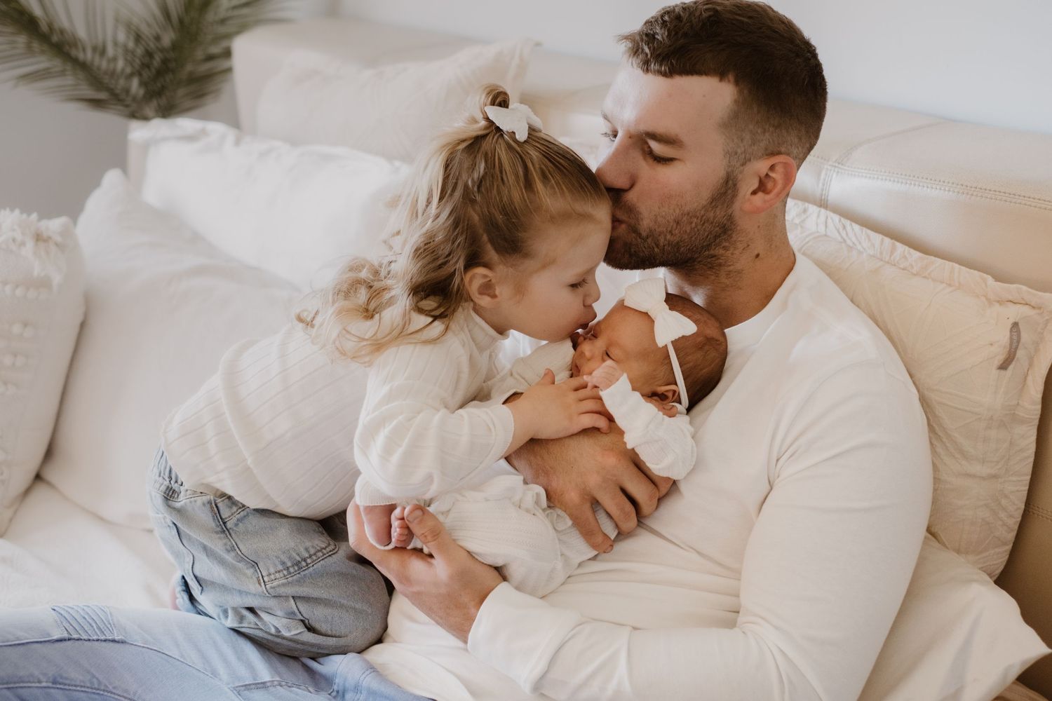 Intimate family moment shared on white bedding in natural light.