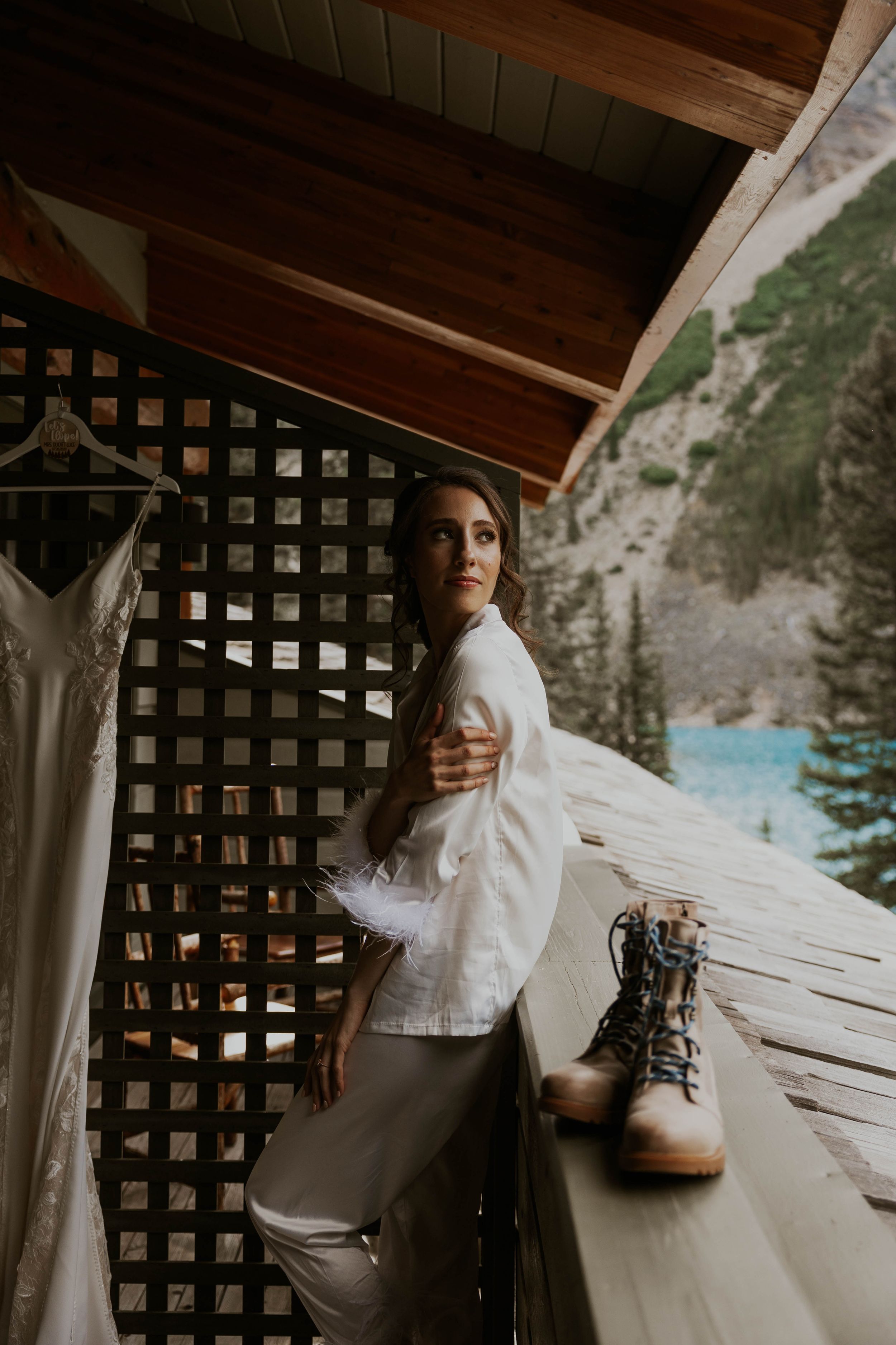 A person in white stands on a wooden deck with mountain scenery and hanging dress visible.