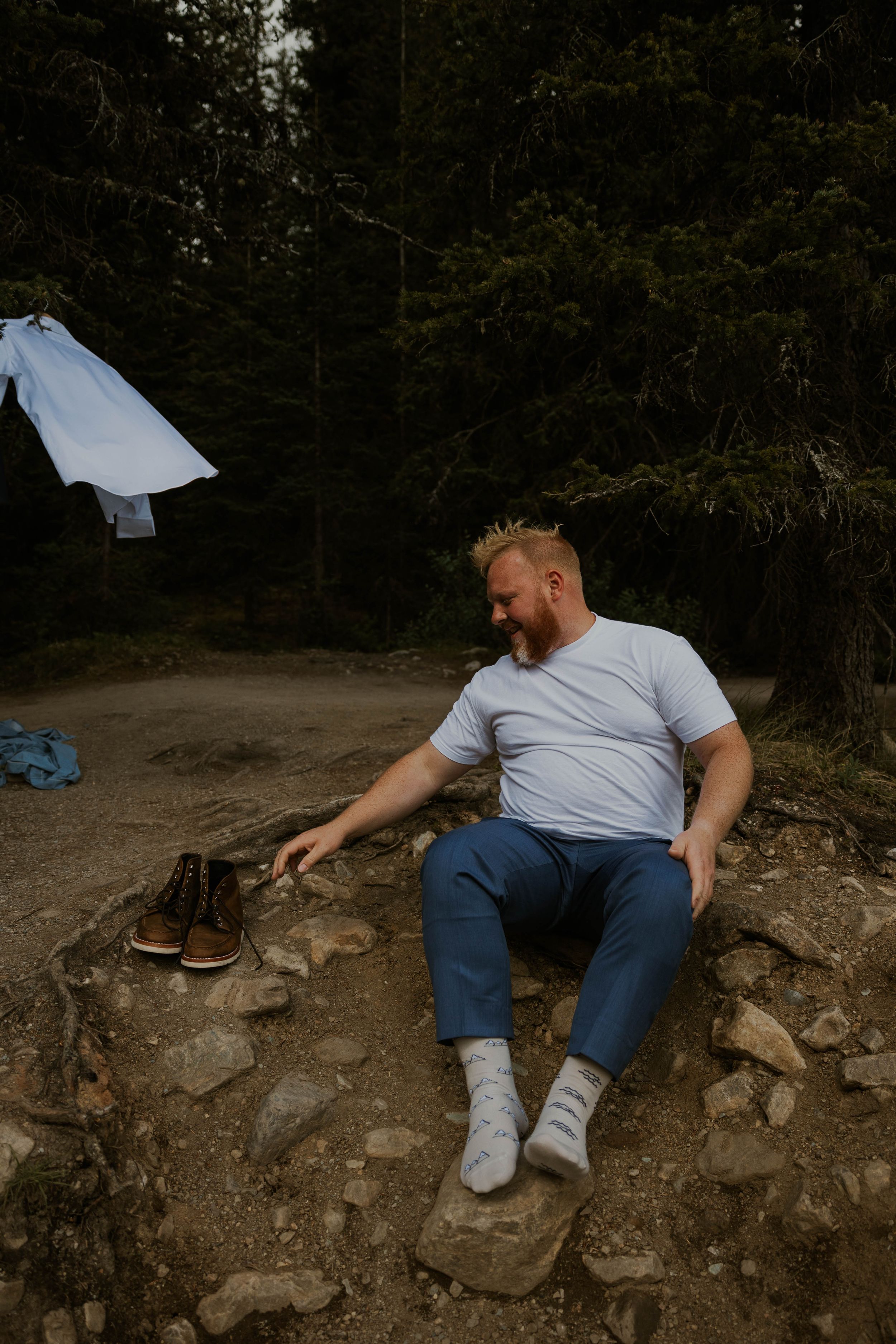 Candid moment showing someone sitting on rocky ground wearing casual clothes in forest setting.
