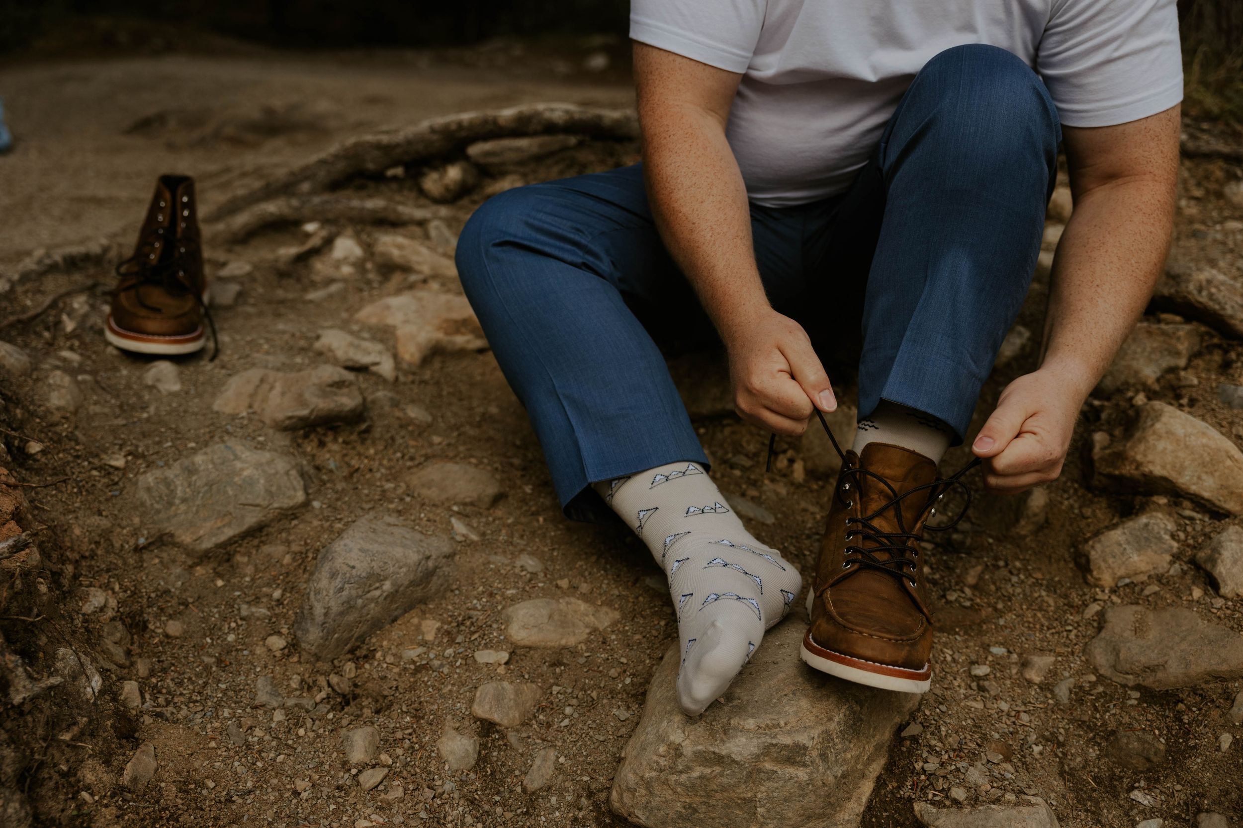 Close-up of brown leather boots being tied on rocky ground with white socks.