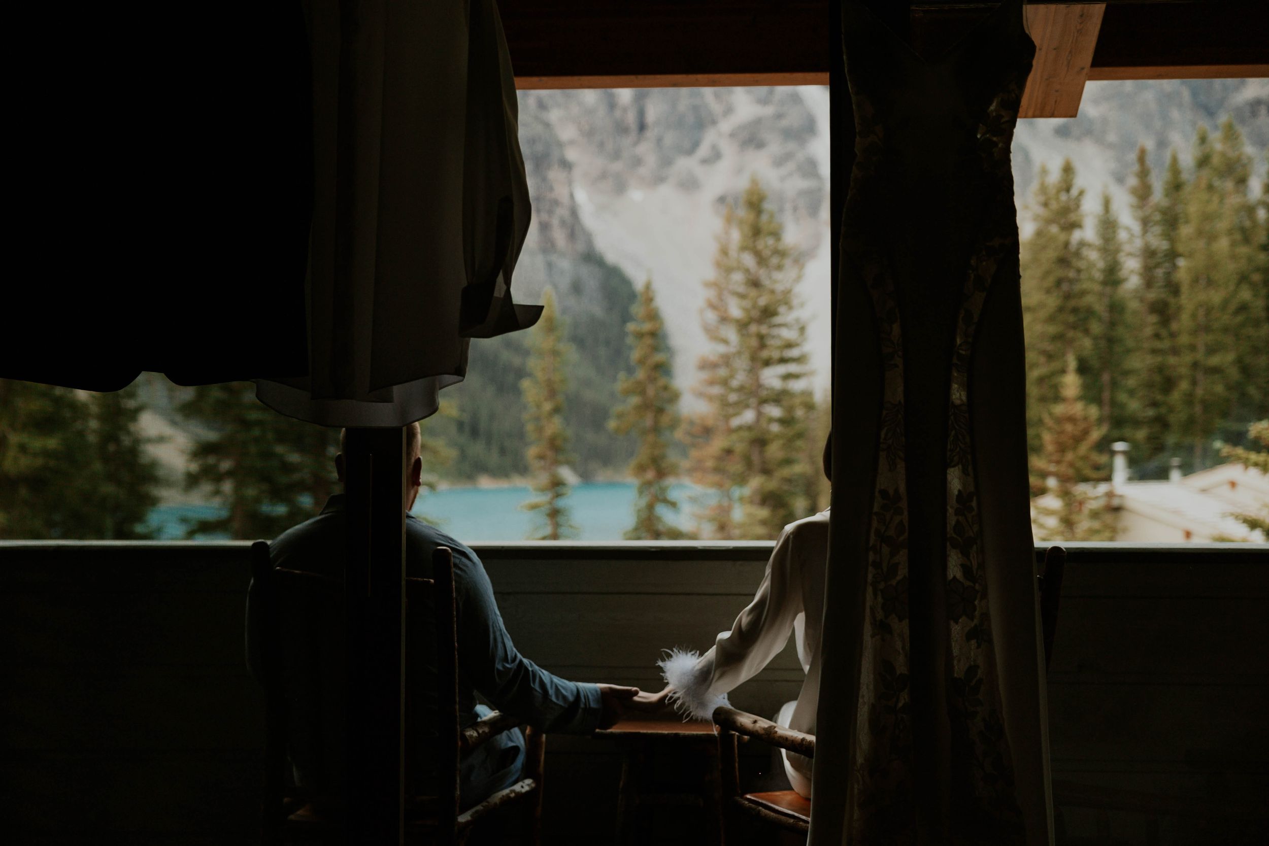 A silhouetted figure gazes out at mountain scenery through a window frame.