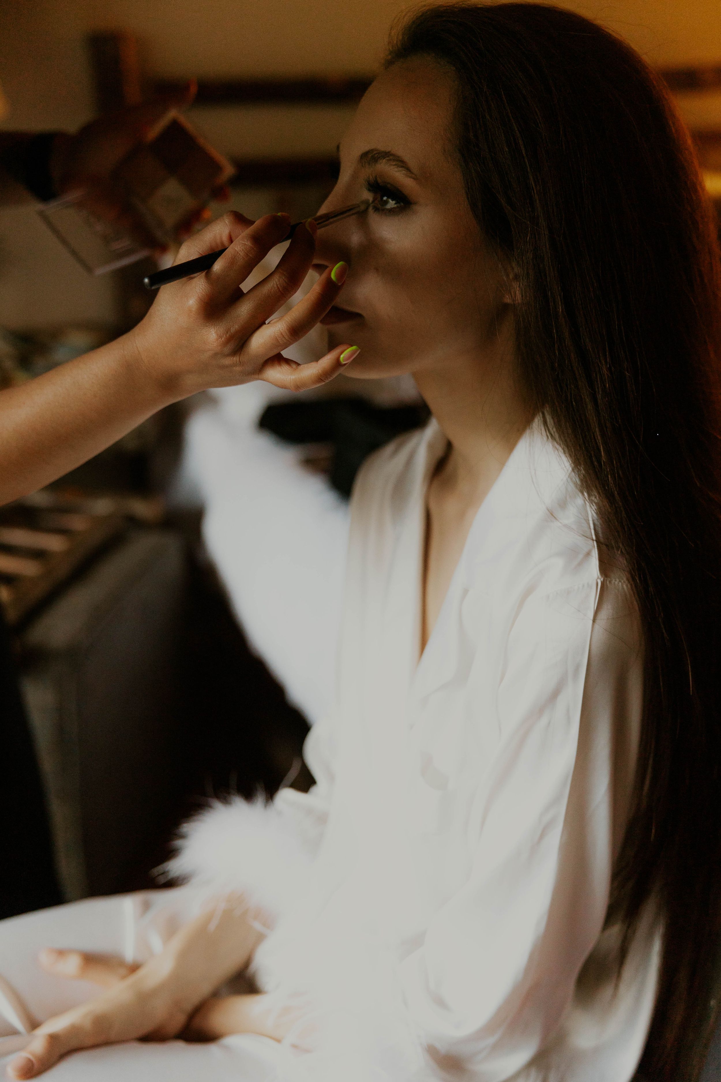 Someone having makeup applied while wearing a white robe in warm lighting.
