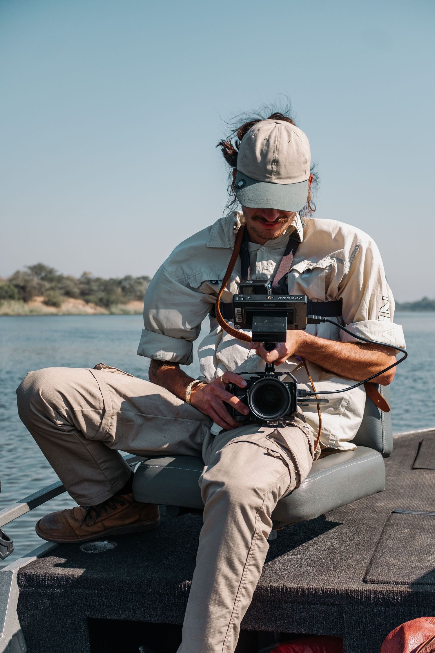 Photographer in light colored clothing reviewing camera footage while sitting on boat deck.