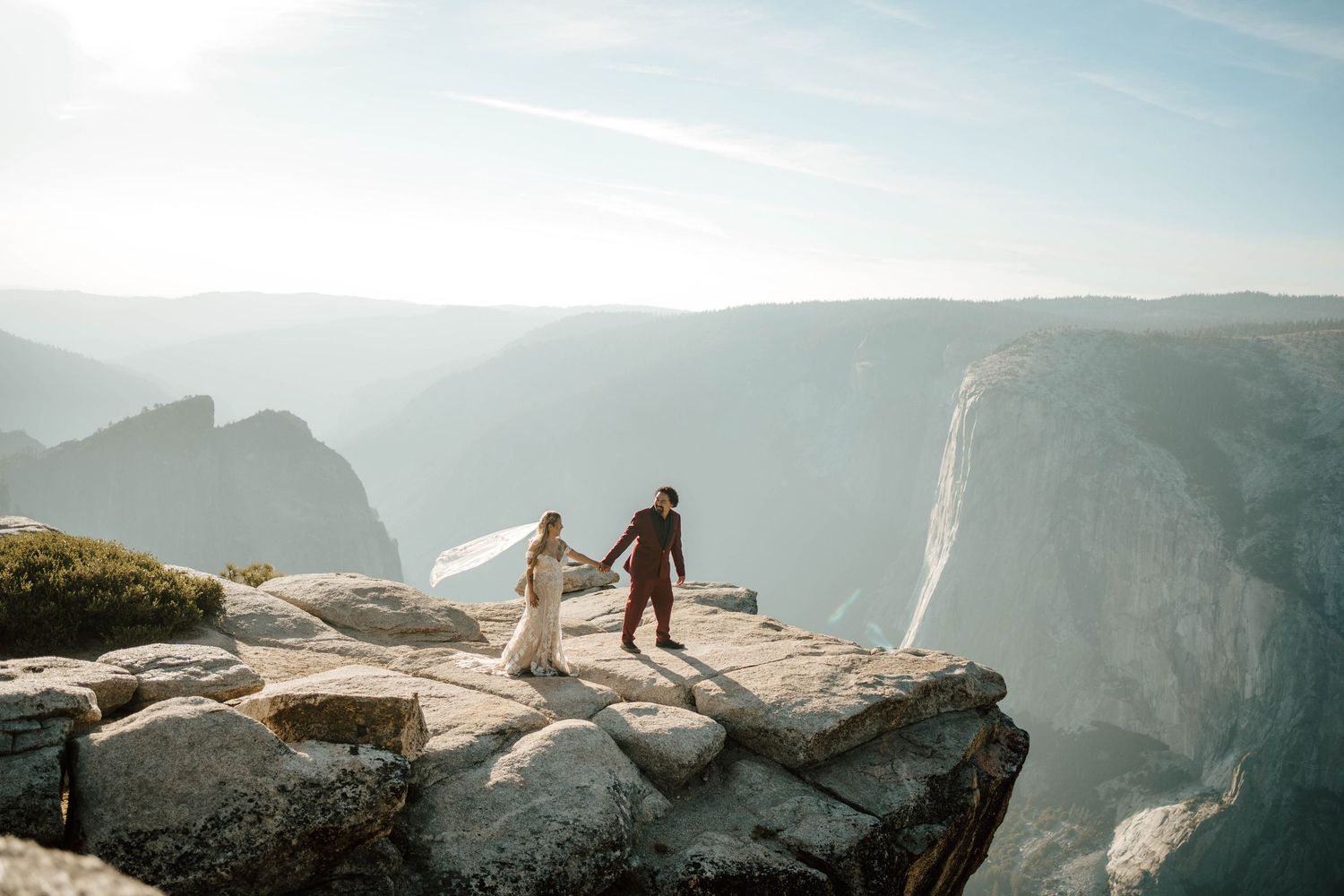Bride and groom hold hands on dramatic Topher Point cliff edge at Yosemite National Park.