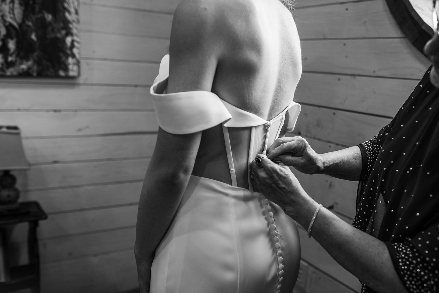 Black and white photo of hands fastening buttons on back of white wedding dress.