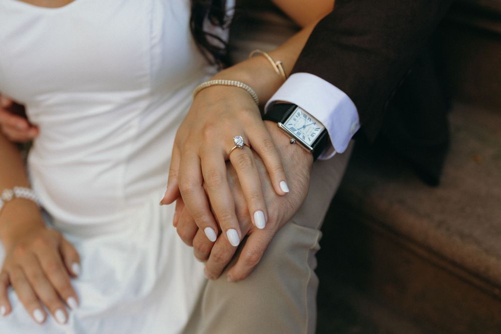 Hands of wedding guests wearing white outfits and rings reach out to touch each other in a celebratory gesture.