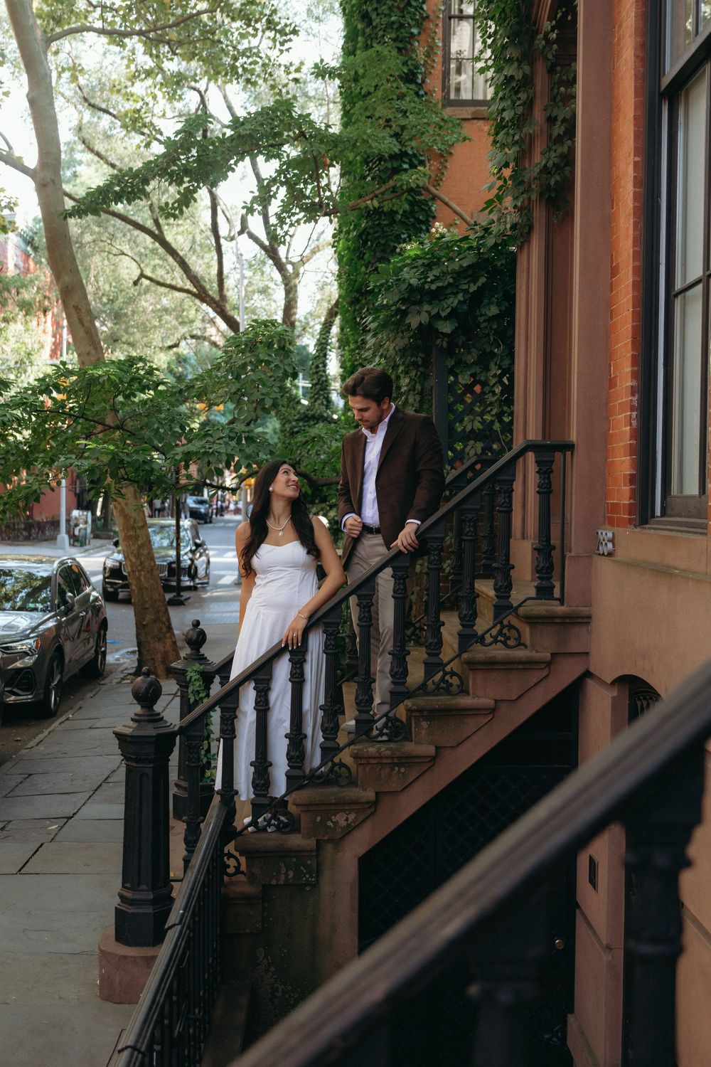 People gathered on a brownstone stoop in a leafy Brooklyn neighborhood on a sunny day.