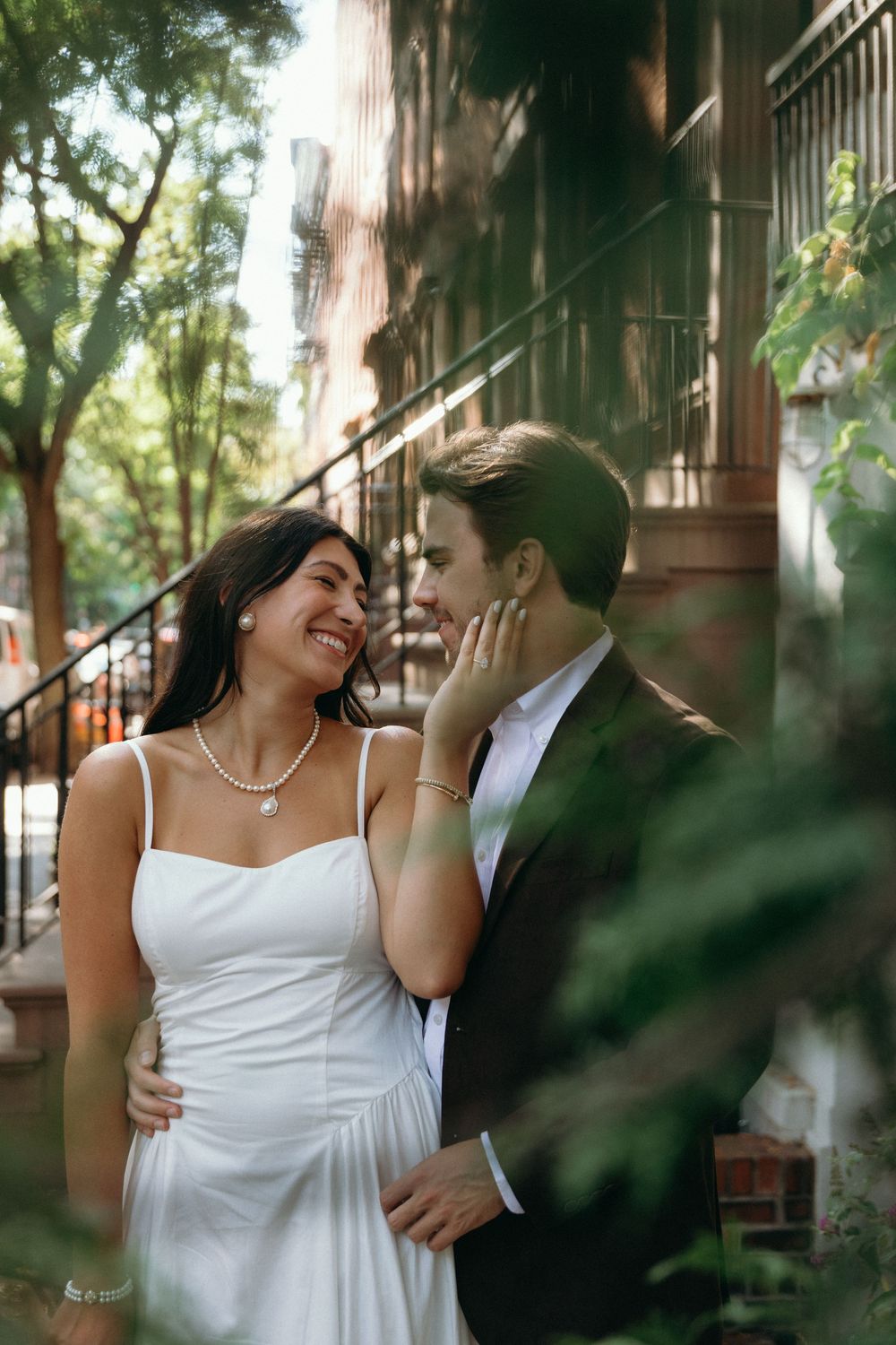 A couple in wedding attire share intimate moments in a garden setting framed by greenery and sunlight.