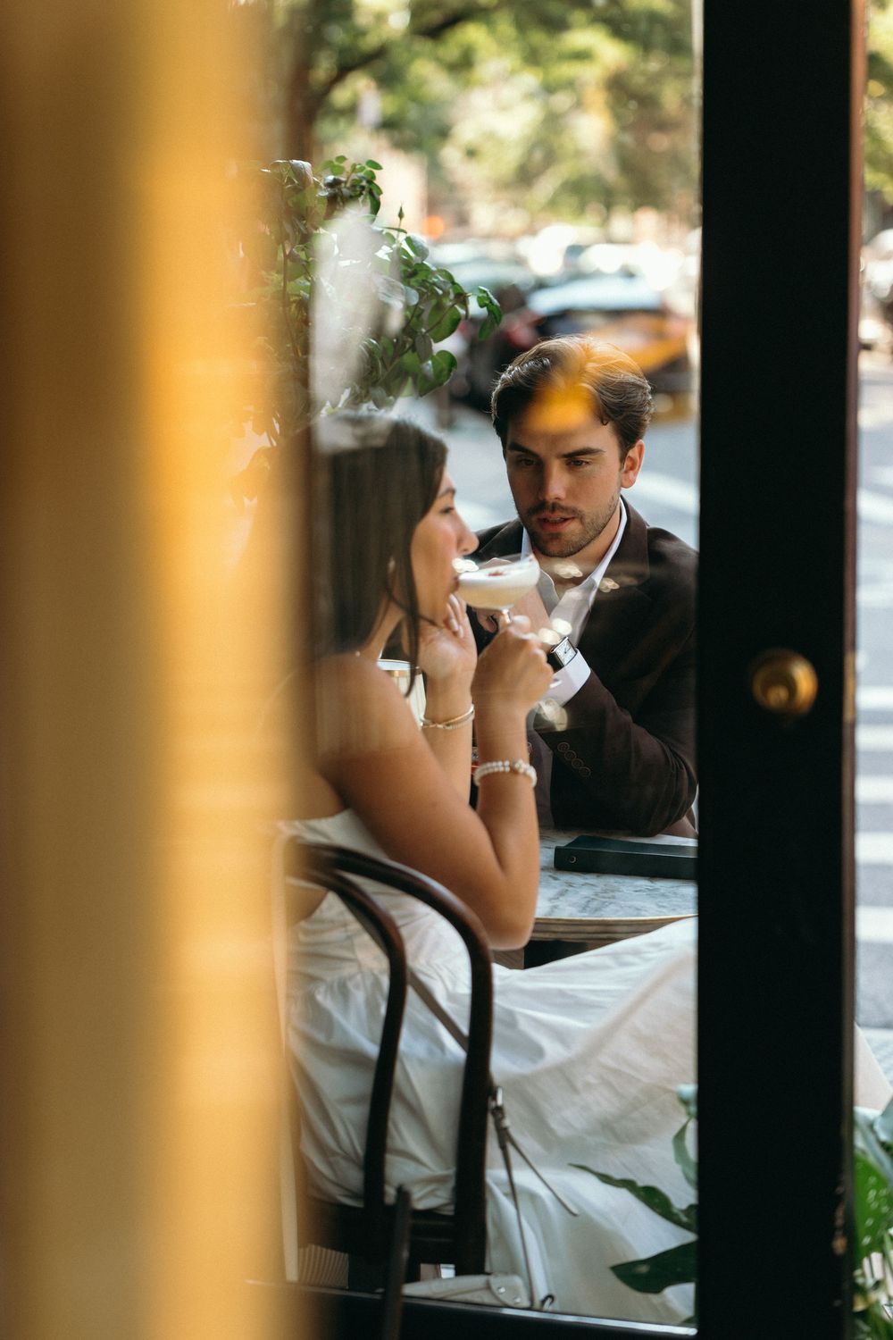 A romantic couple shares an intimate moment at a restaurant table viewed through window blinds.