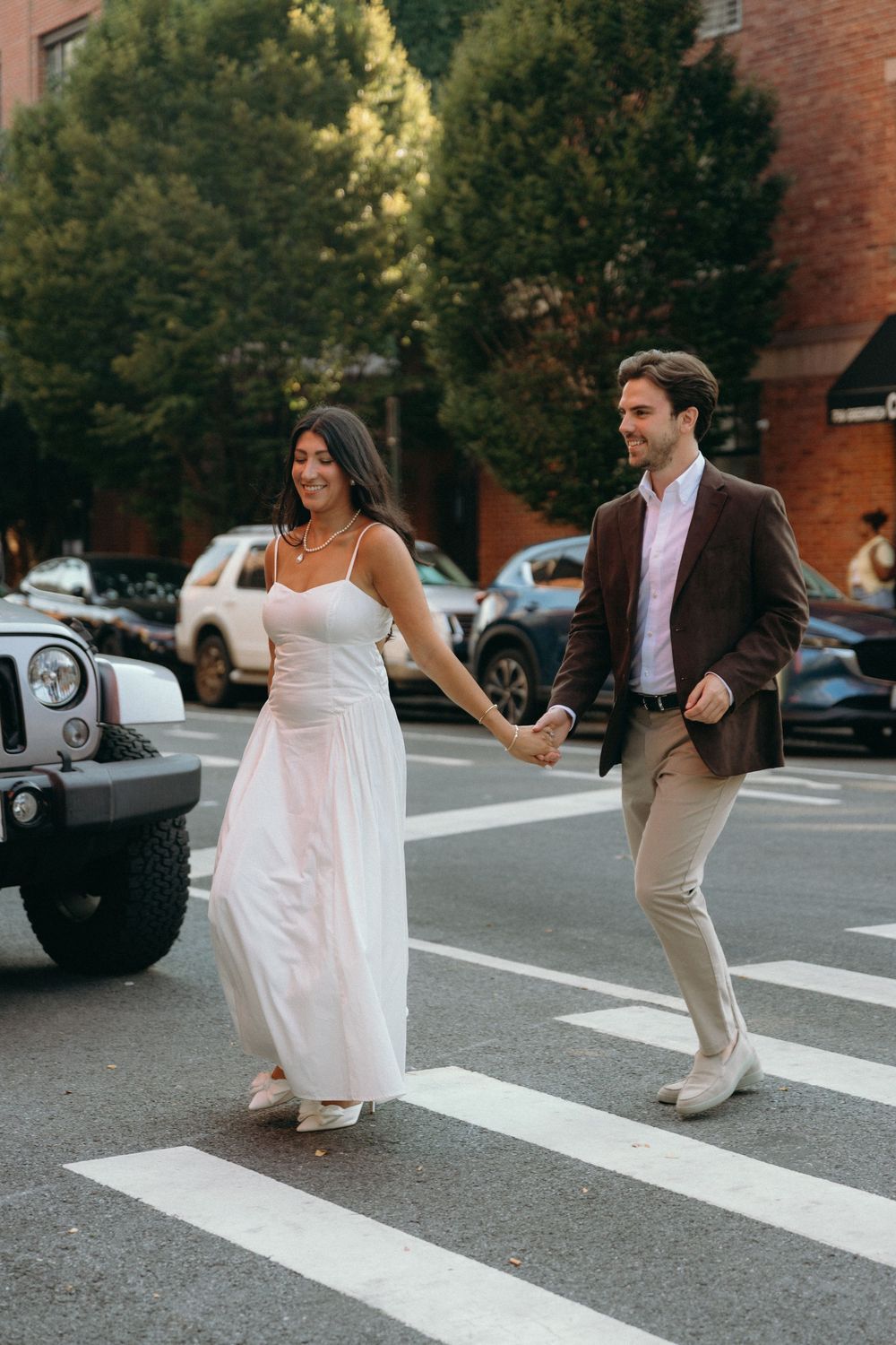 People playfully crossing a crosswalk in front of an ivy-covered brick building.