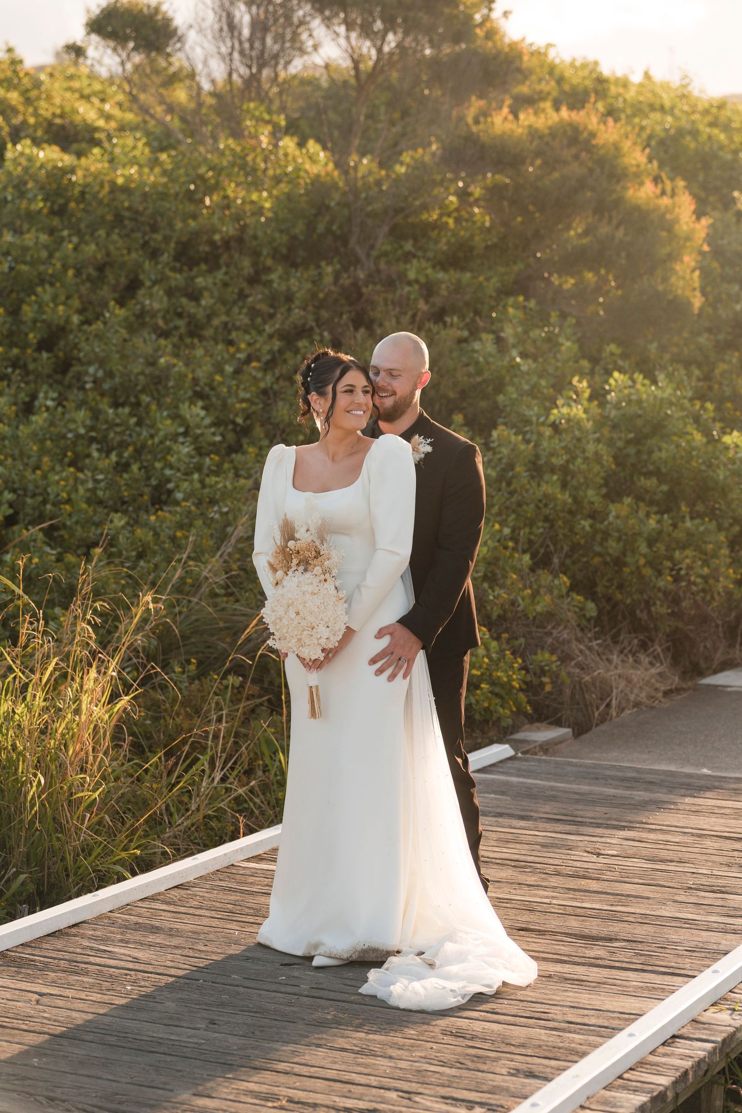 Couple sharing romantic moments at sunset on a wooden boardwalk surrounded by lush greenery.