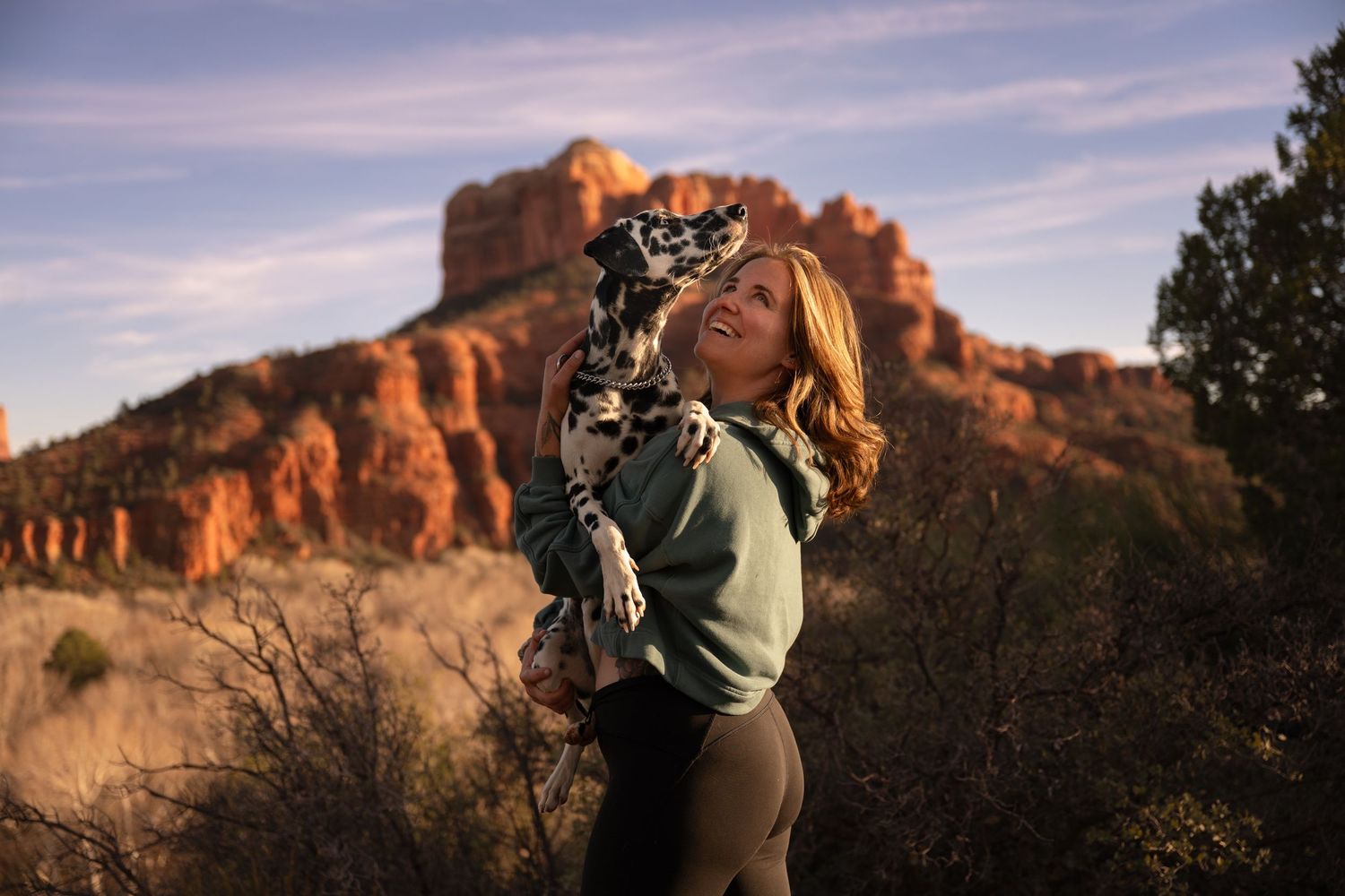 A young woman holds her dog at sunset in front of Cathedral Rock in Sedona, Arizona.