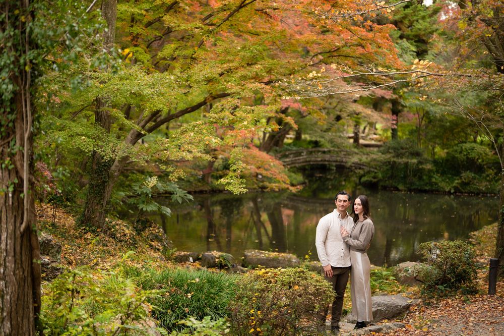 Couple poses together near a tranquil pond surrounded by colorful autumn foliage in a Japanese garden.