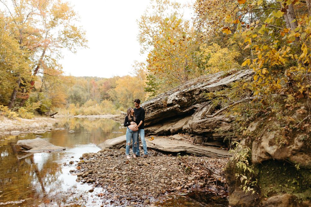 Autumn trees with golden leaves line a peaceful river bank with large rocks and boulders along the shore.