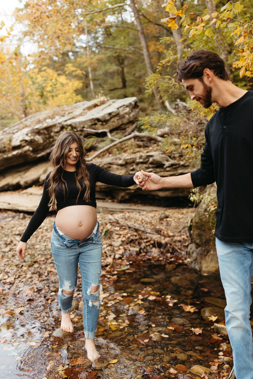 A couple shares tender moments by a rocky creek surrounded by fall foliage.