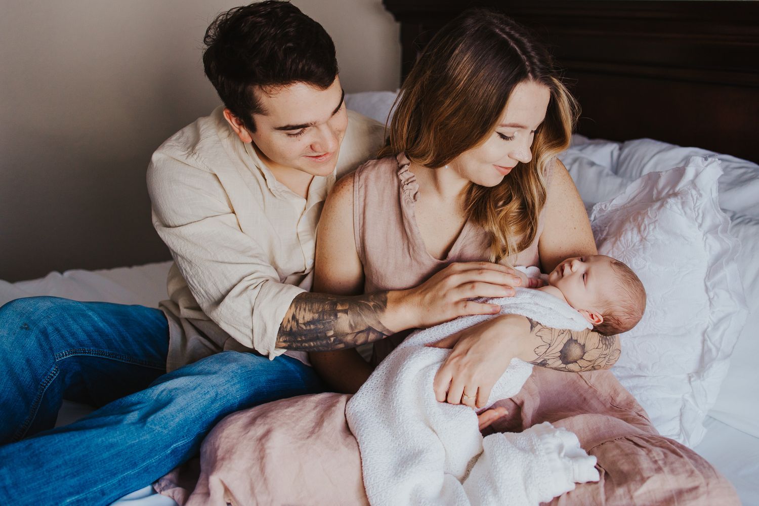 Intimate lifestyle newborn photography session with parents and baby on white bedding.