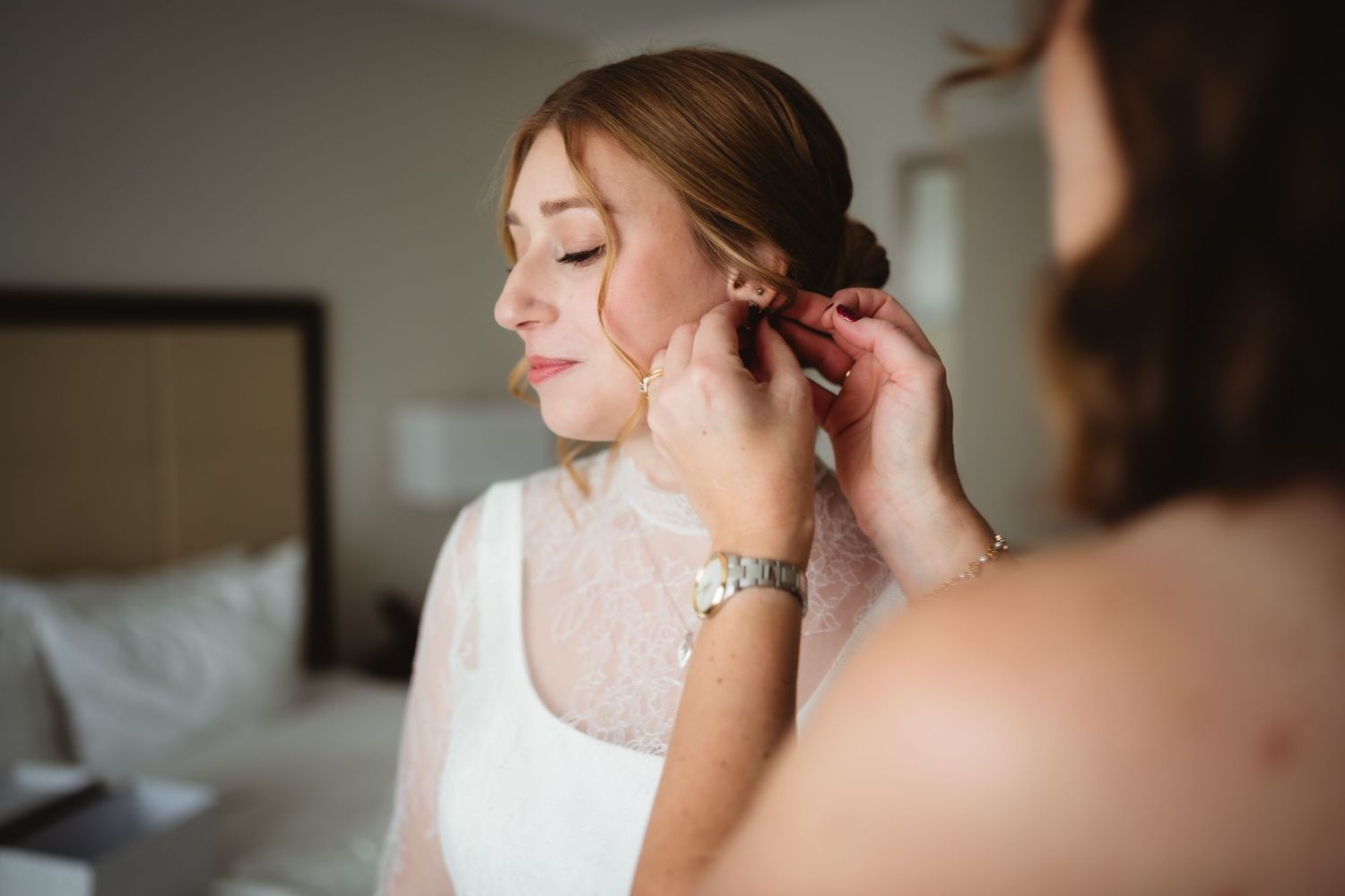 Close-up view of someone putting on elegant pearl drop earrings while wearing a delicate white lace dress.
