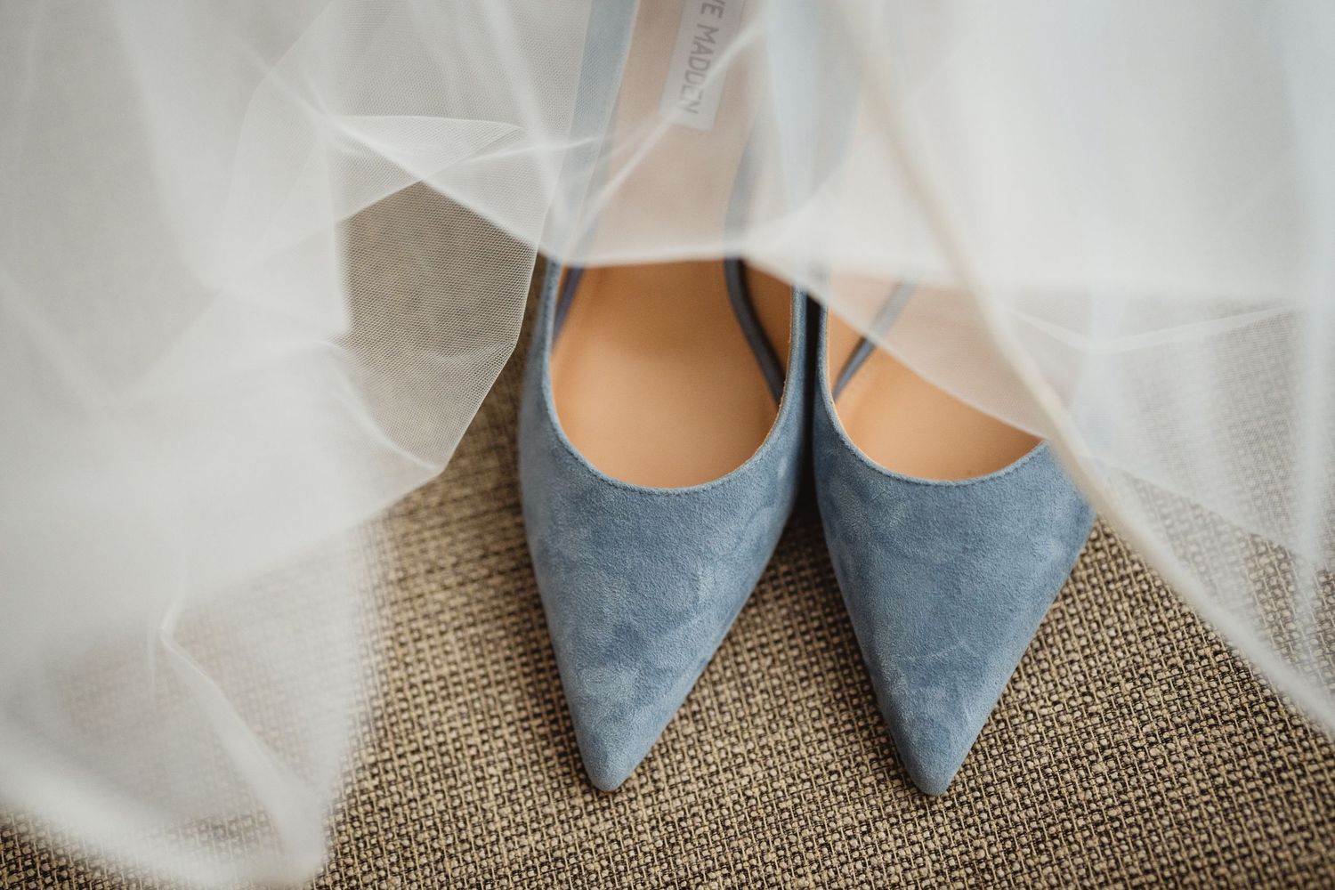 Close-up view of elegant blue suede pointed-toe shoes against a light carpet background.