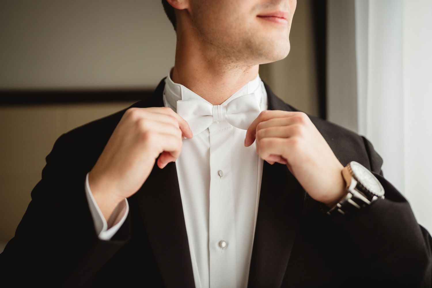 Person in formal attire adjusts their white collar and bowtie while getting dressed.