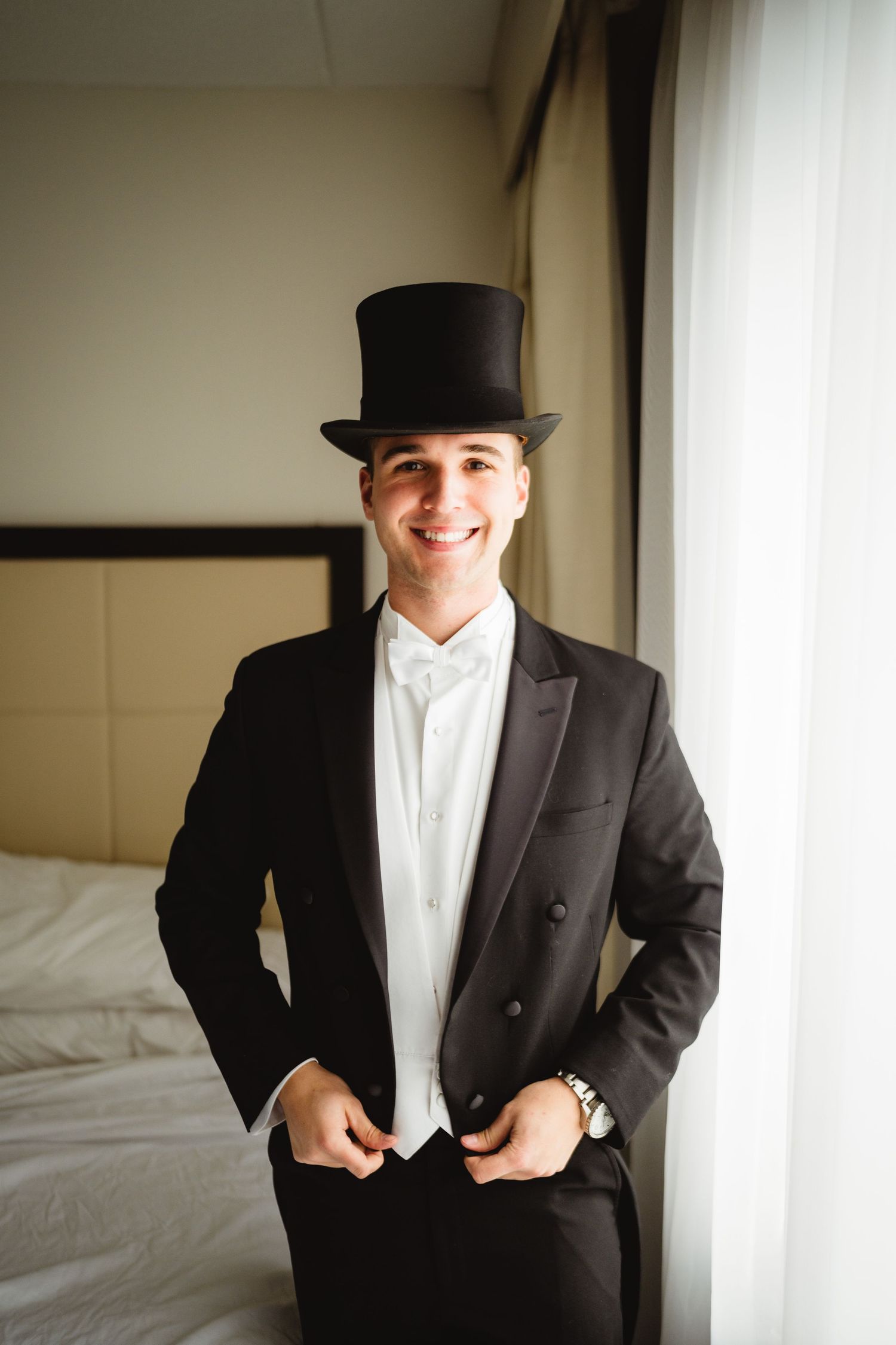 Formal black tuxedo with white dress shirt and top hat in a bright interior setting.